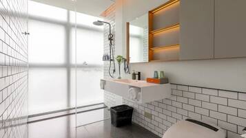 Et moderne badeværelse med en glasbrusekabine, et hvidt håndvaskarrangement med et spejl, og et hvidt toilet.