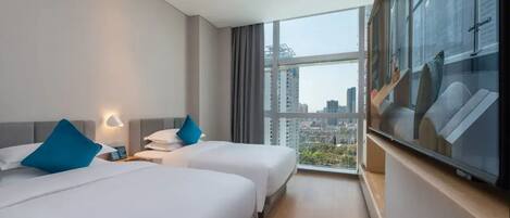Quarto de hotel com duas camas, uma janela grande com vista para a cidade e uma televisão de tela plana em um suporte.
