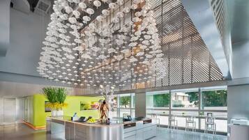 A modern hotel lobby with a central reception desk, large windows, and a ceiling adorned with hanging white umbrellas.