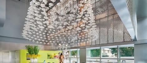 A modern hotel lobby with a central reception desk, large windows, and a ceiling adorned with hanging white umbrellas.
