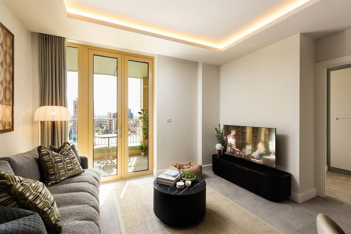 Una sala de estar moderna con un sofá, una mesa de centro, un televisor y un balcón con vistas a edificios.