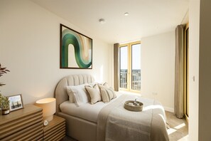 Ein modernes Schlafzimmer mit einem großen Bett, einem Nachttisch, einem gerahmten Bild und einem Fenster mit Ausblick.