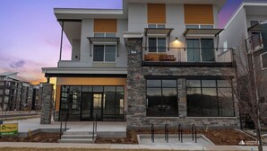 A modern two-story building with a stone facade, large windows, and a balcony with outdoor seating. - Modern Apartment + Balcony (Fort Collins)