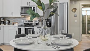 A modern kitchen with white cabinetry, a stainless steel refrigerator, and a dining table set for four with plates, glasses, and cutlery. - Modern Apartment + Balcony (Fort Collins)