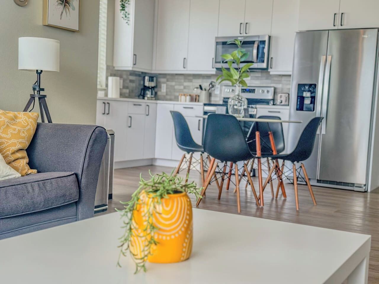 A modern living room with a grey sofa, a coffee table with a plant, and a dining area with a white table and blue chairs.