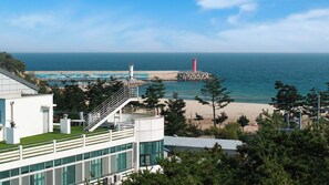 Un hotel frente al mar, con vista a la playa, un faro y un rompeolas rocoso.