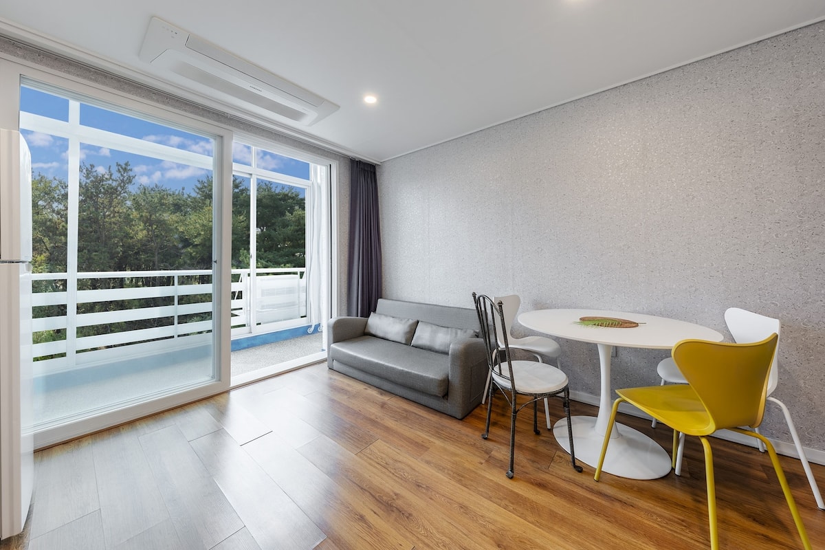 A modern living room with a grey sofa, a round white table, and yellow chairs.