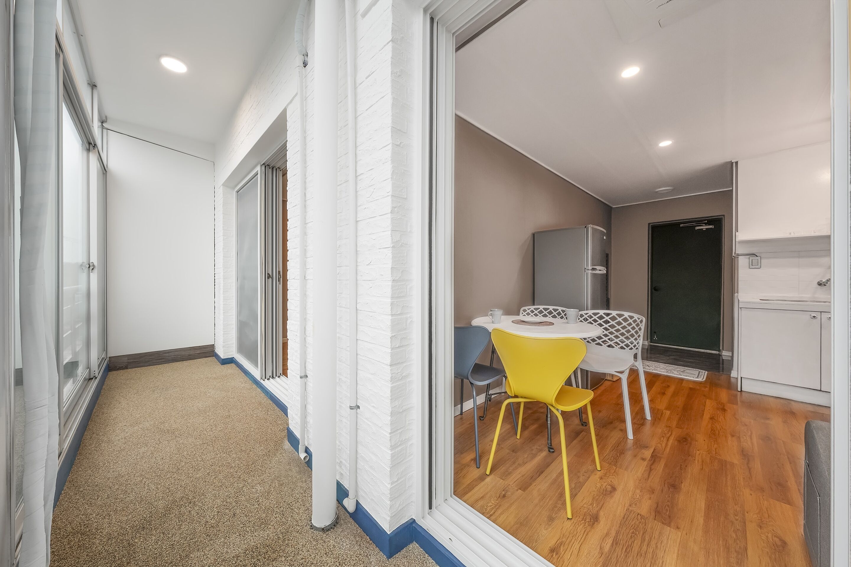 A modern kitchen with white cabinetry, a yellow chair, and a small dining table.