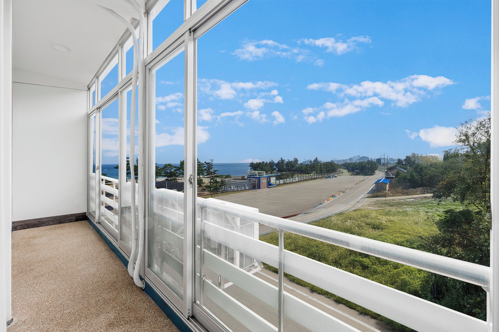 A balcony with a view of a road and greenery, a white railing, and a clear sky.