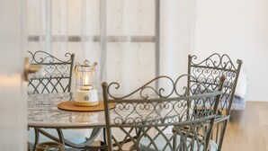 A dining table with a glass top, surrounded by metal chairs with intricate designs. A table lamp is placed on the table, and a woven placemat is visible.