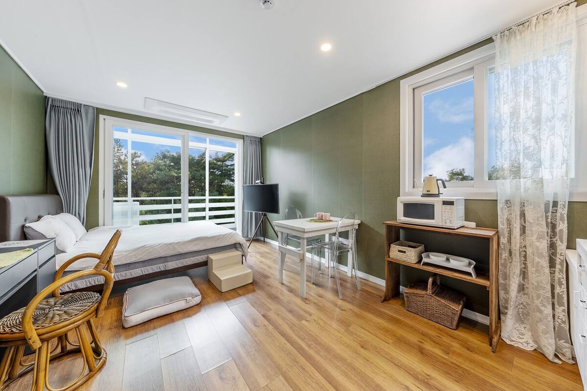 A bedroom with a bed, bedside table, TV, and a view of the outdoors.