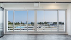 A spacious balcony with large sliding glass doors, offering a view of a beach and a distant cityscape.
