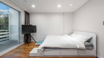Un dormitorio moderno con cama, televisor sobre un mueble bajo y puerta corrediza de vidrio a un balcón.