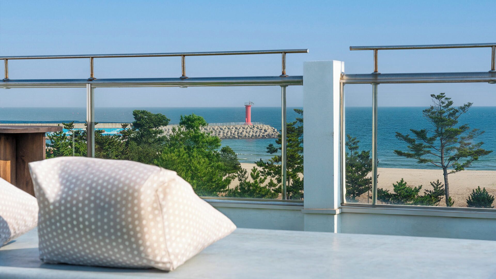 A room with a view of a beach, a lighthouse, and a rocky outcrop.