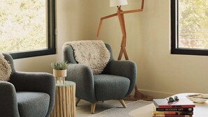 Um quarto aconchegante com duas poltronas, um abajur e uma mesinha com livros e uma planta.