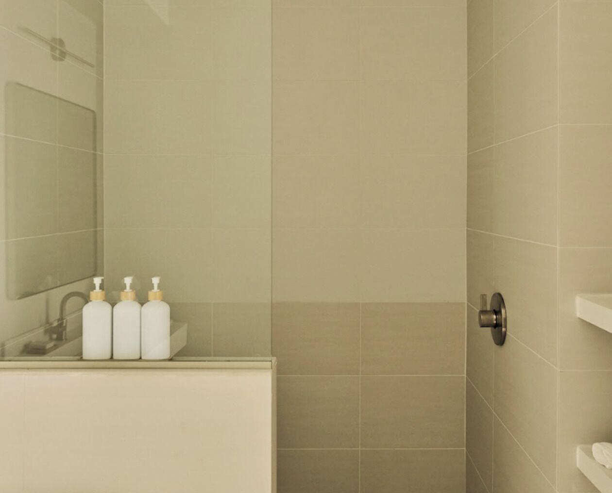 A bathroom with a mirror, sink, three bottles, and a shower door.