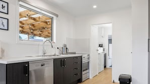 A modern kitchen with a dishwasher, oven, and microwave. There is a window with wooden beams and string lights. - Fantastic Family Lakehouse - Room for everyone (Mangakino)