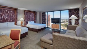 Habitación de hotel con cama extragrande, dos camas dobles, un sofá, televisión y vistas a la ciudad.