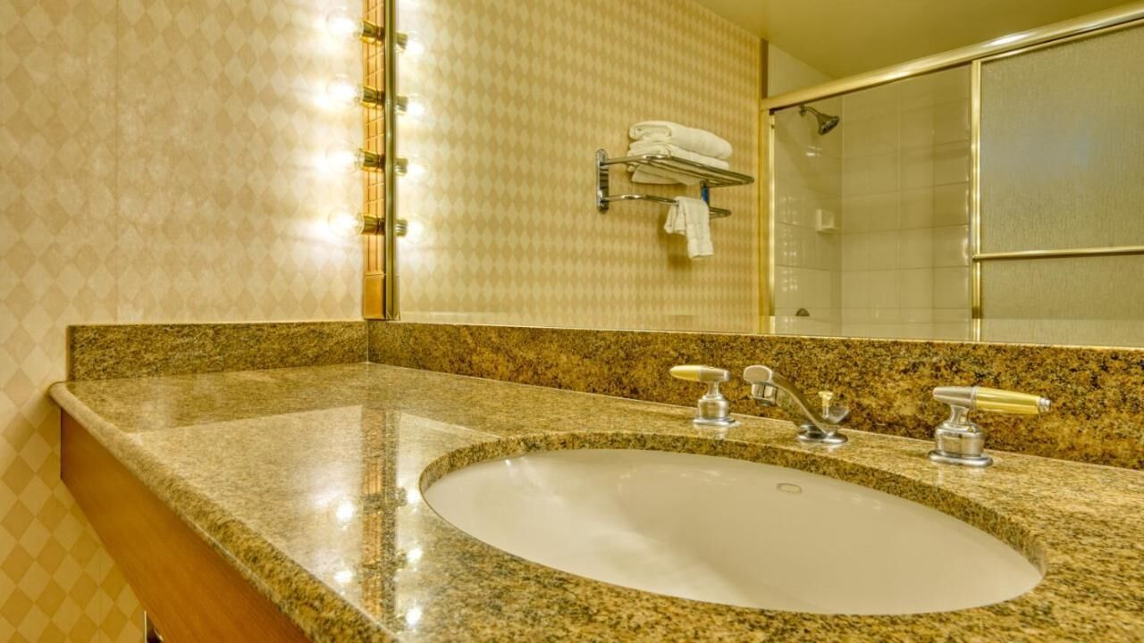 A bathroom with a granite countertop sink, a mirror, and a towel rack with folded towels.
