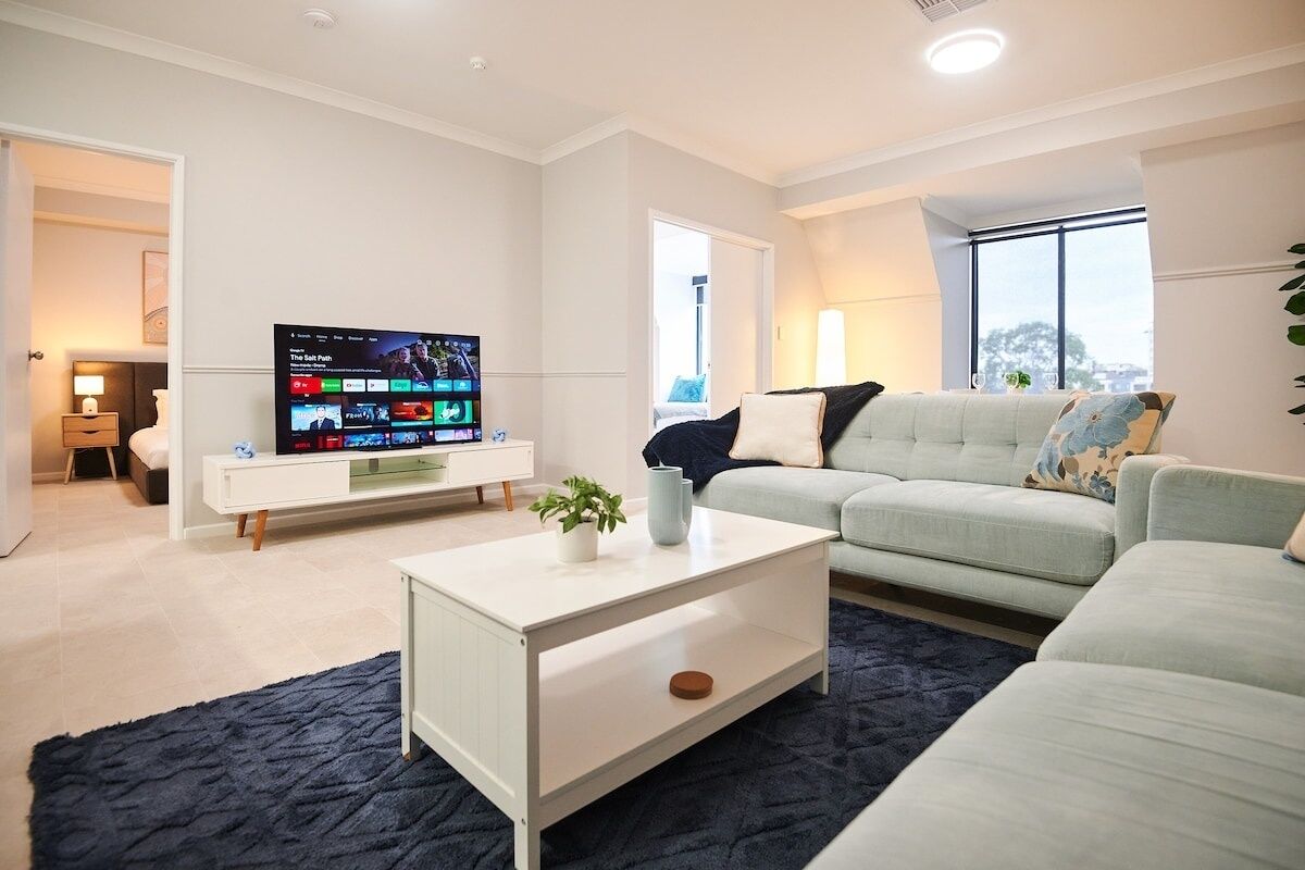 Un salon moderne avec un téléviseur à écran plat, un canapé de couleur claire, une table basse et un tapis foncé.