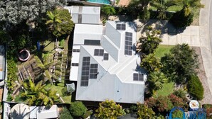 Eine Luftaufnahme eines Wohngebiets mit mehreren Häusern, von denen einige mit Solaranlagen ausgestattet sind, umgeben von Grünflächen und Palmen.