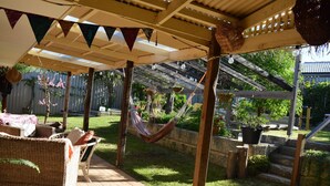 Ein überdachter Patio-Bereich mit Rattanmöbeln, einer Hängematte und Topfpflanzen.