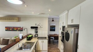 Eine kompakte Küche mit weißen Schränken, einem Edelstahlkühlschrank und einem Essbereich mit Tisch und Stühlen.