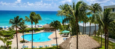 A resort with a pool, palm trees, and a view of the ocean.