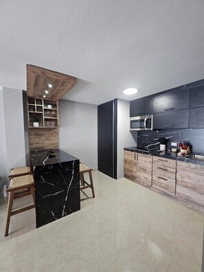 A modern kitchen with a black marble countertop, wooden cabinets, and a built-in microwave. - Eduardo's Home (San Juan)