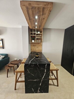 A modern kitchen with a black marble island, wooden stools, and a built-in shelf unit. - Eduardo's Home (San Juan)
