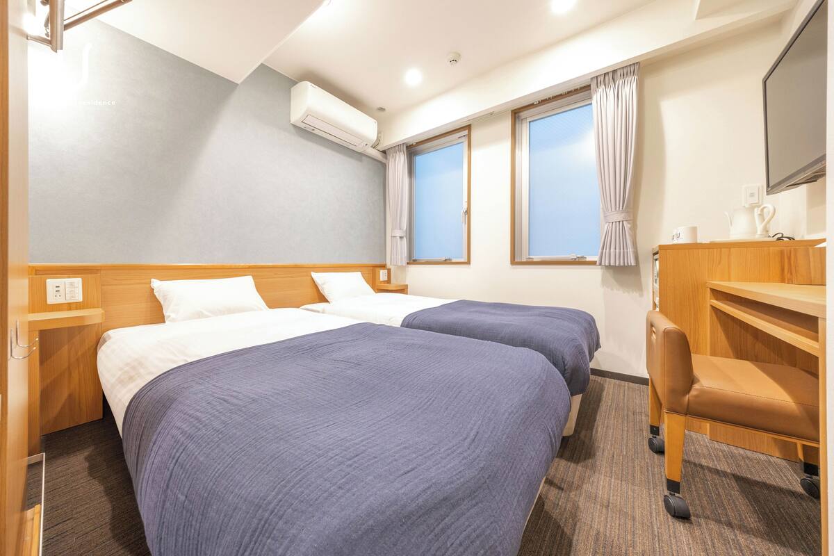 A hotel room with two beds, a desk, and a chair.