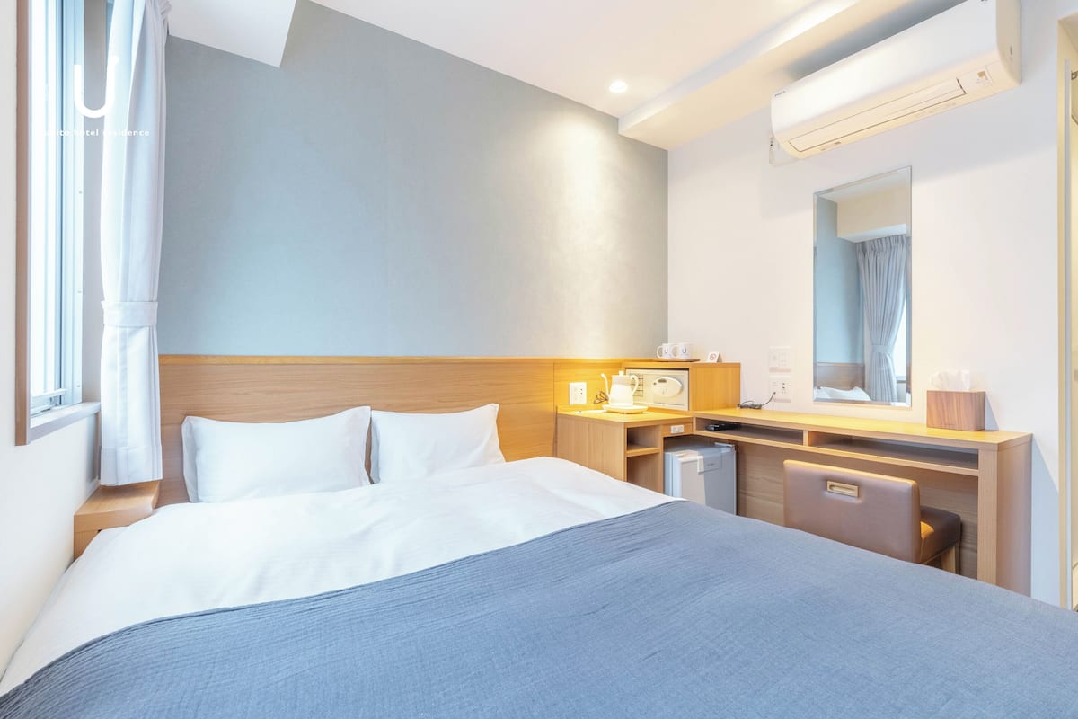 A hotel room with a bed, bedside table, desk, chair, and a mirror.