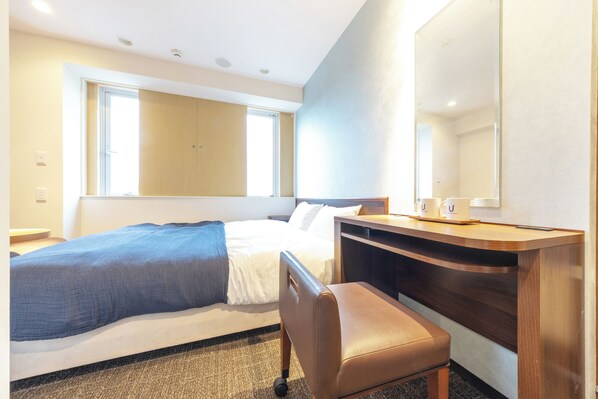Habitación de hotel con cama, escritorio, silla, un espejo grande y ventana.
