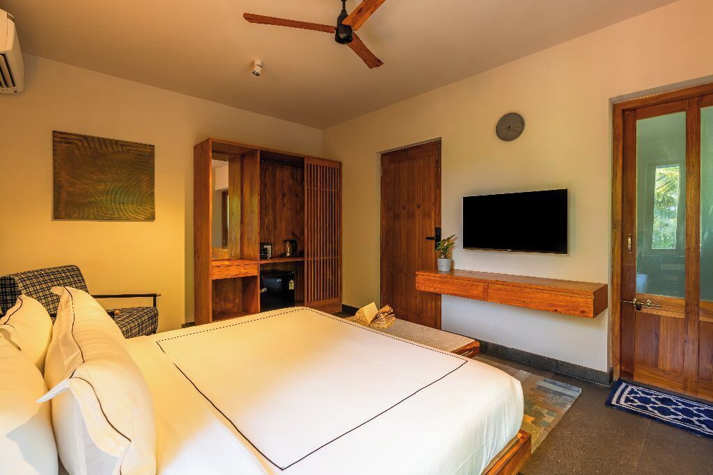 A bedroom with a bed, a ceiling fan, a TV mounted on the wall, and wooden furniture.