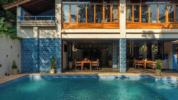 Una casa a due piani con piscina, zona pranzo all'aperto e portico coperto.