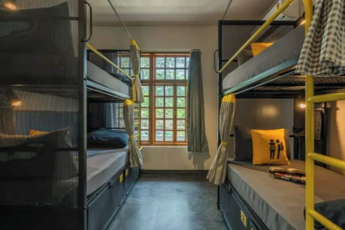 A dormitory room with bunk beds, a window with curtains, and a small table with a book.
