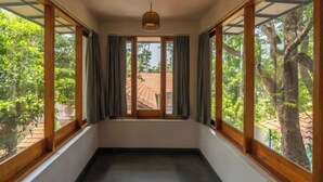 Ein Zimmer mit großen Fenstern, einer Deckenleuchte und Blick auf Bäume und ein Gebäude.