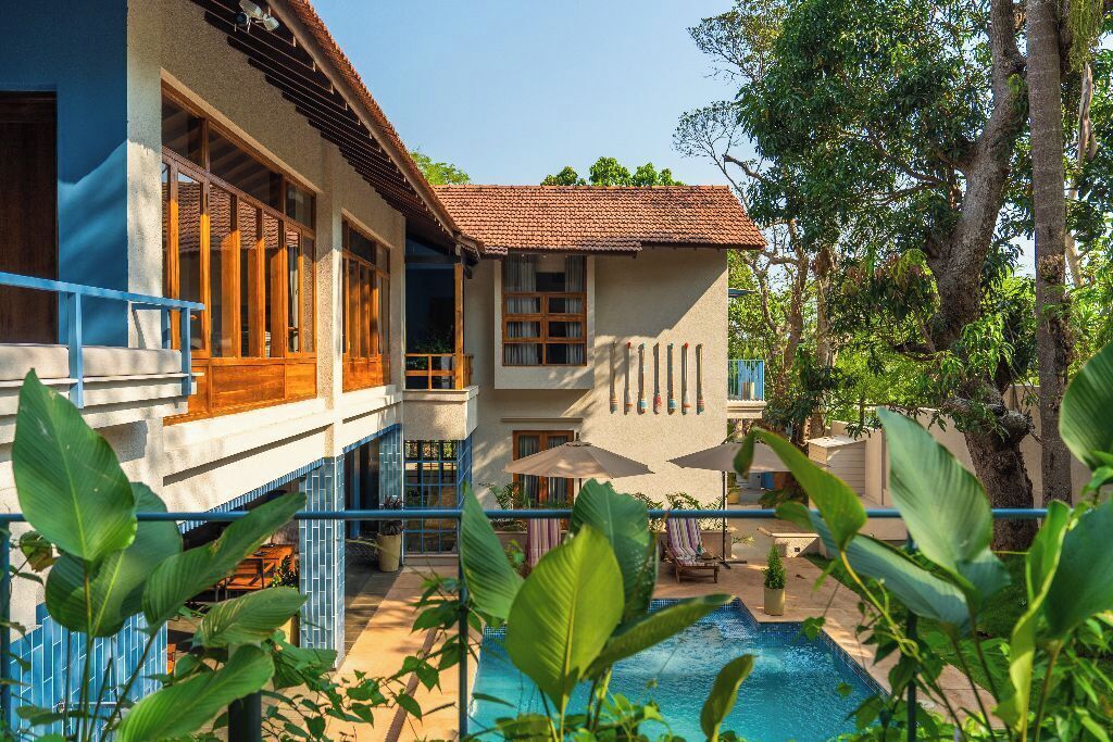 Una casa de dos pisos con piscina, rodeada de abundante vegetación.