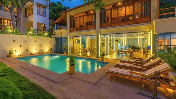 Ein modernes, zweistöckiges Haus mit Swimmingpool, Außenbereich zum Sitzen und gut beleuchtetem Innenraum.