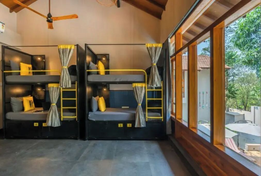 A room with bunk beds, a ceiling fan, and a large window with a view of the outdoors.