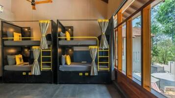 A room with bunk beds, a ceiling fan, and a large window with a view of the outdoors.