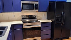Une cuisine moderne avec des meubles bleus, un four à micro-ondes en acier inoxydable, un four et un réfrigérateur noir.