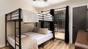 A bunk bed room with a ceiling fan, a wooden floor, and a sliding glass door leading to an outdoor area. - Modern Table Rock Cabin - Close to Lake and SDC! (Kimberling City)