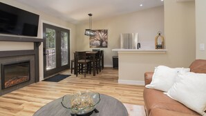 A living room with a fireplace, a dining area, and a kitchen with a bar. - Modern Table Rock Cabin - Close to Lake and SDC! (Kimberling City)