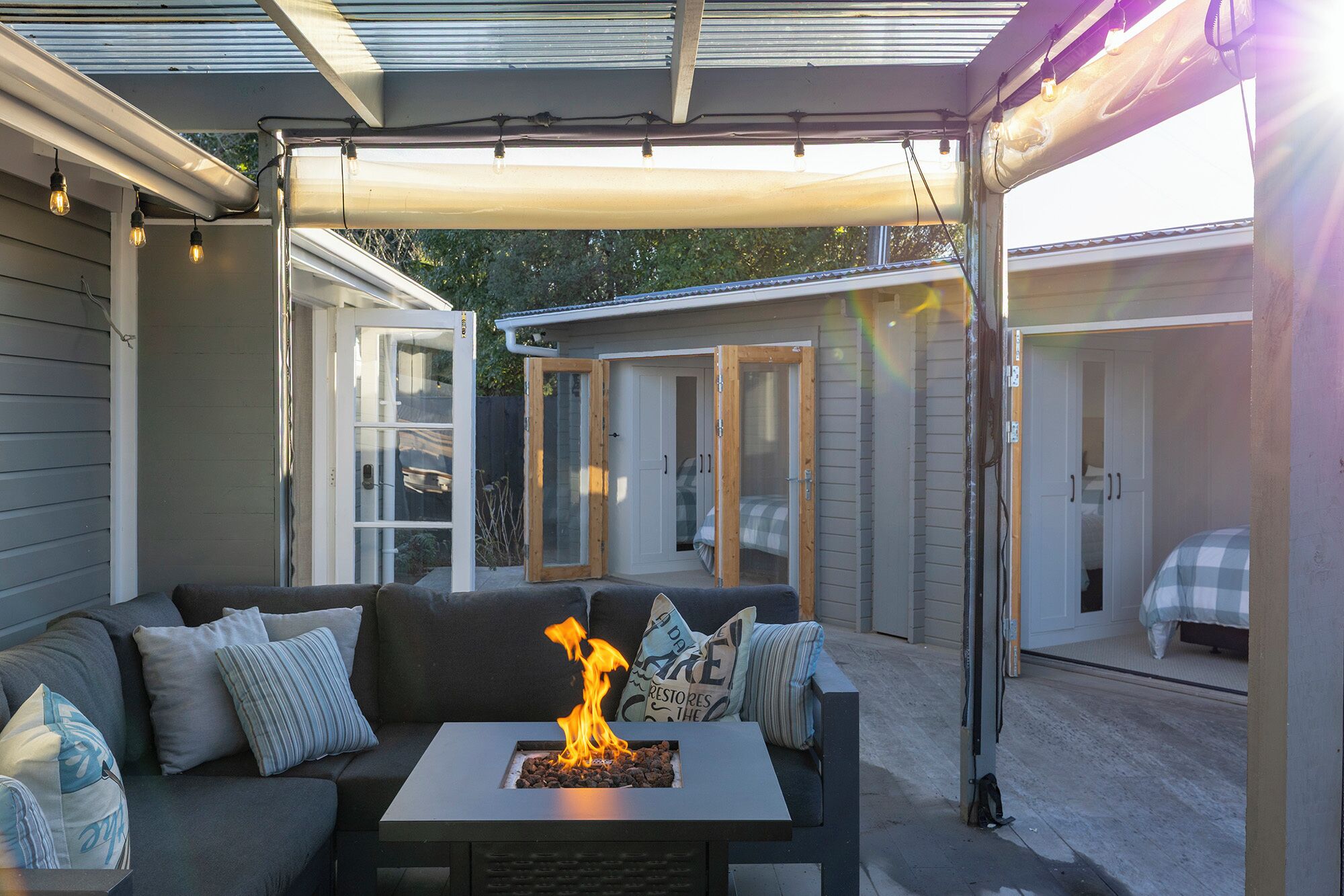 Een terras buiten met een vuurplaats, een bank en een overdekt gedeelte met deuren naar slaapkamers.