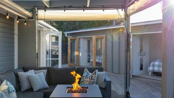 Een terras buiten met een vuurplaats, een bank en een overdekt gedeelte met deuren naar slaapkamers.