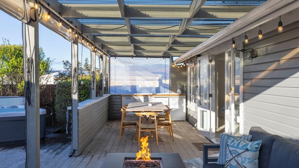 A covered outdoor patio with a fire pit, wooden furniture, and a view of a house. - Luxury Hideaway at the Lake (Mangakino)