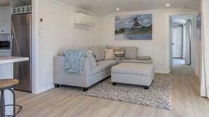 A modern kitchen with a stainless steel refrigerator, a grey sofa with a throw blanket, and a painting of a water scene on the wall. - Luxury Hideaway at the Lake (Mangakino)
