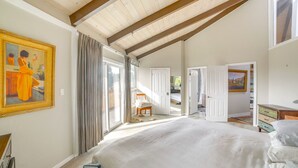 A bedroom with a large bed, a painting on the wall, a chair, and a door leading to another room. - Redwood Retreat Near Beach & Trails (Aptos)
