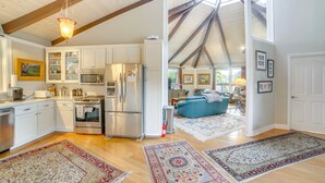 A spacious kitchen with modern appliances, a dining area with a blue sofa, and a living room with a large window. - Redwood Retreat Near Beach & Trails (Aptos)